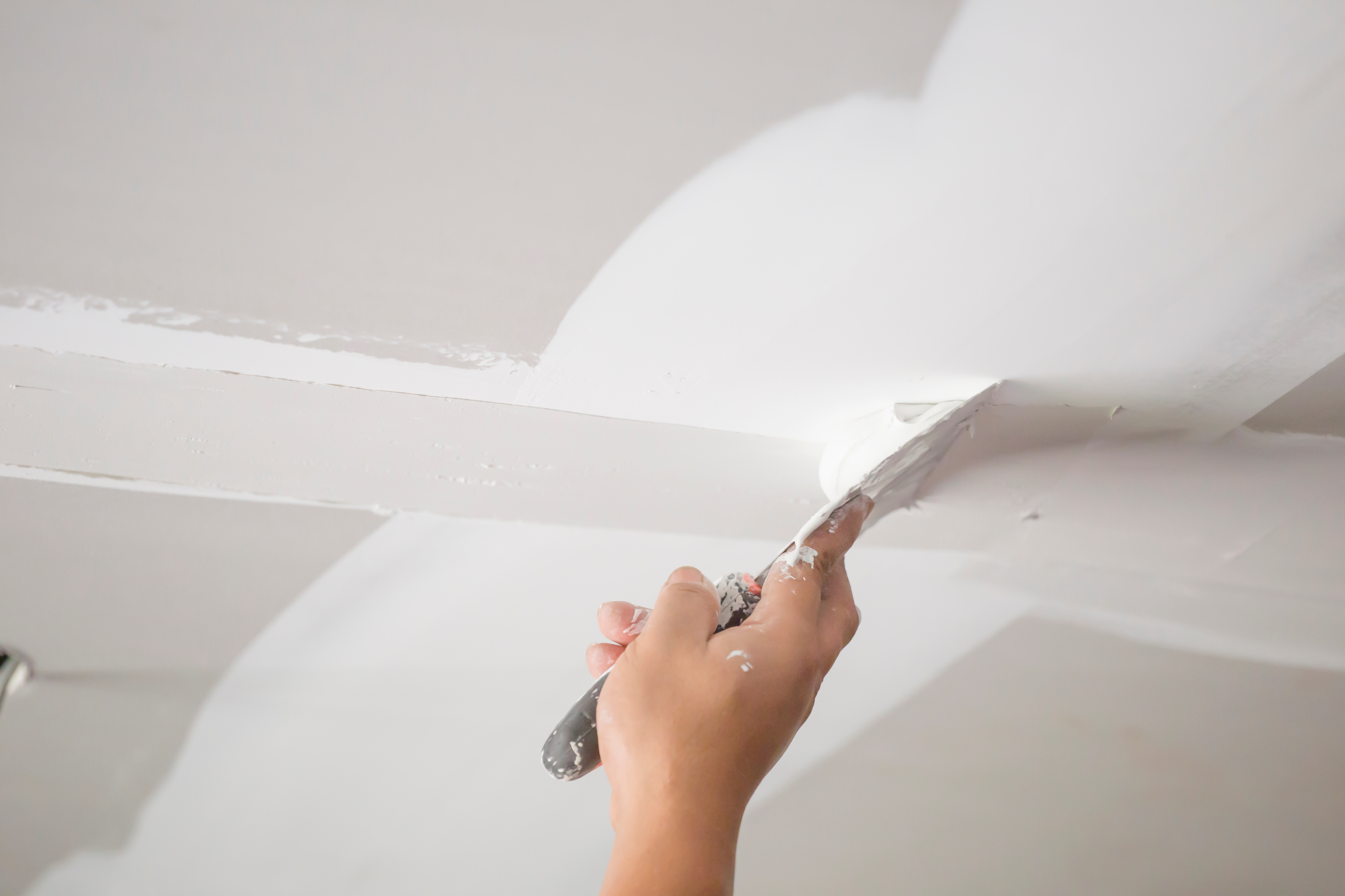 Worker applying joint compound to drywall ceiling with putty knife
