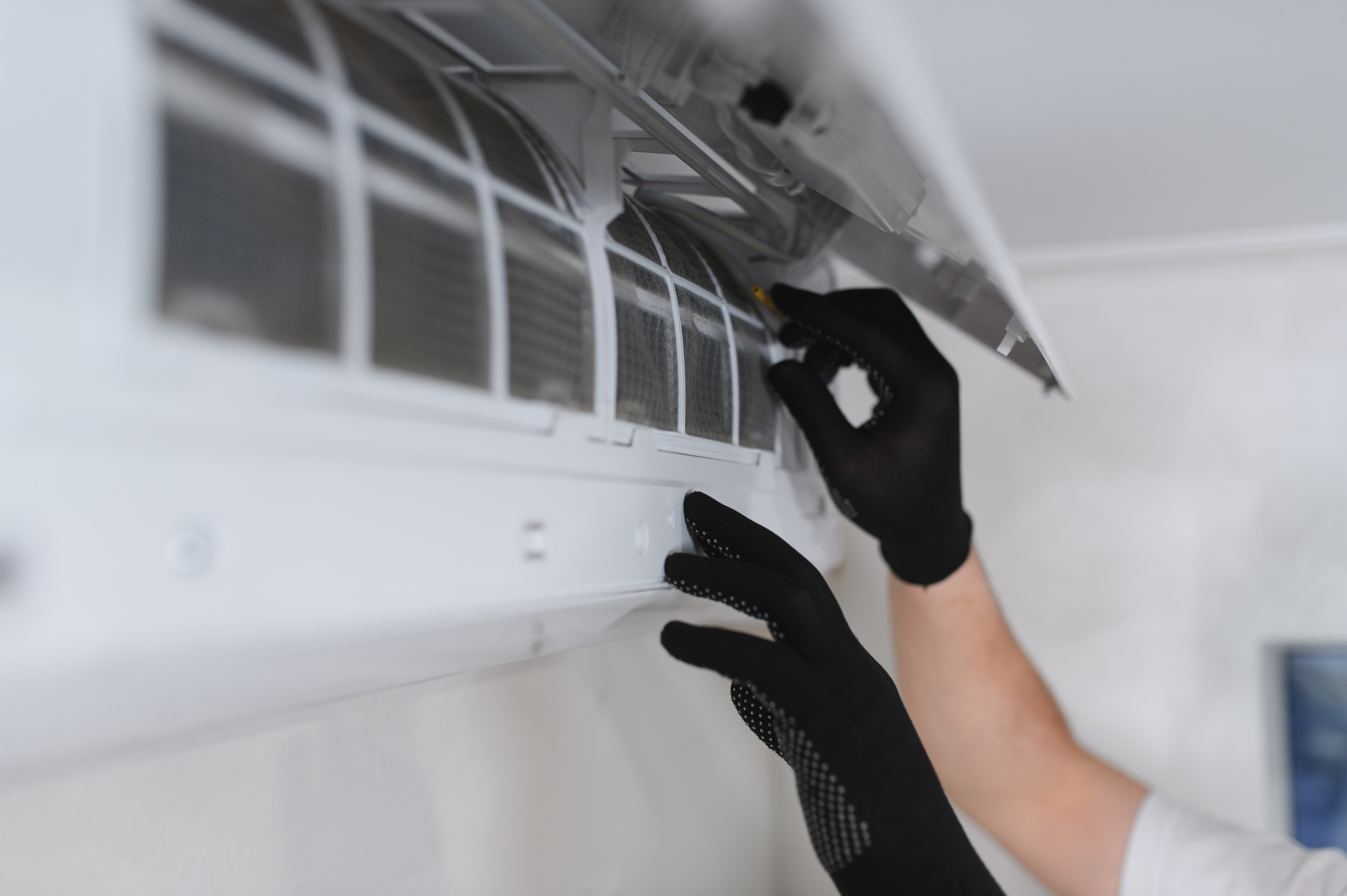 Technician in black gloves cleaning white air conditioning unit indoors
