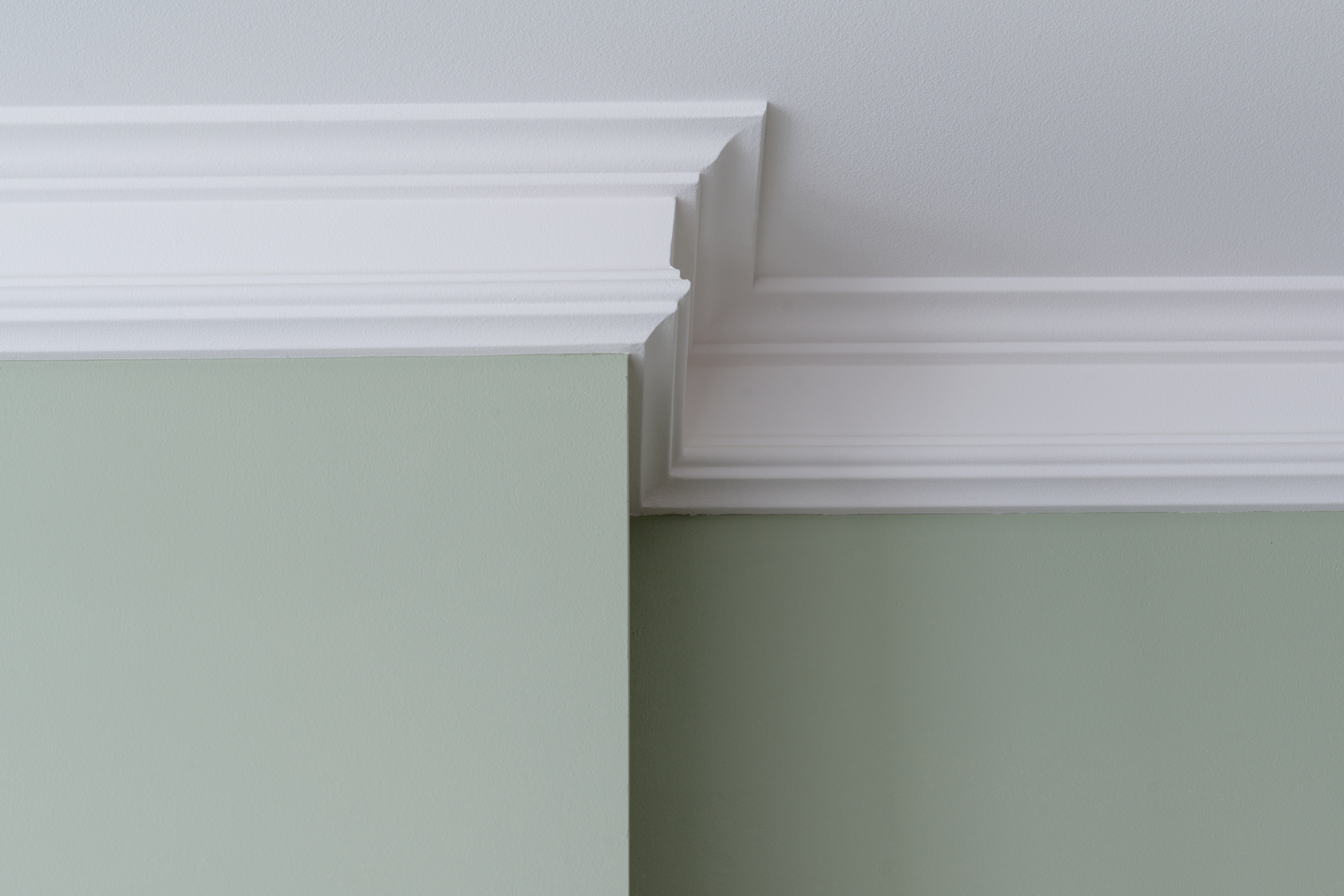 White decorative crown molding installed where pale green wall meets gray ceiling