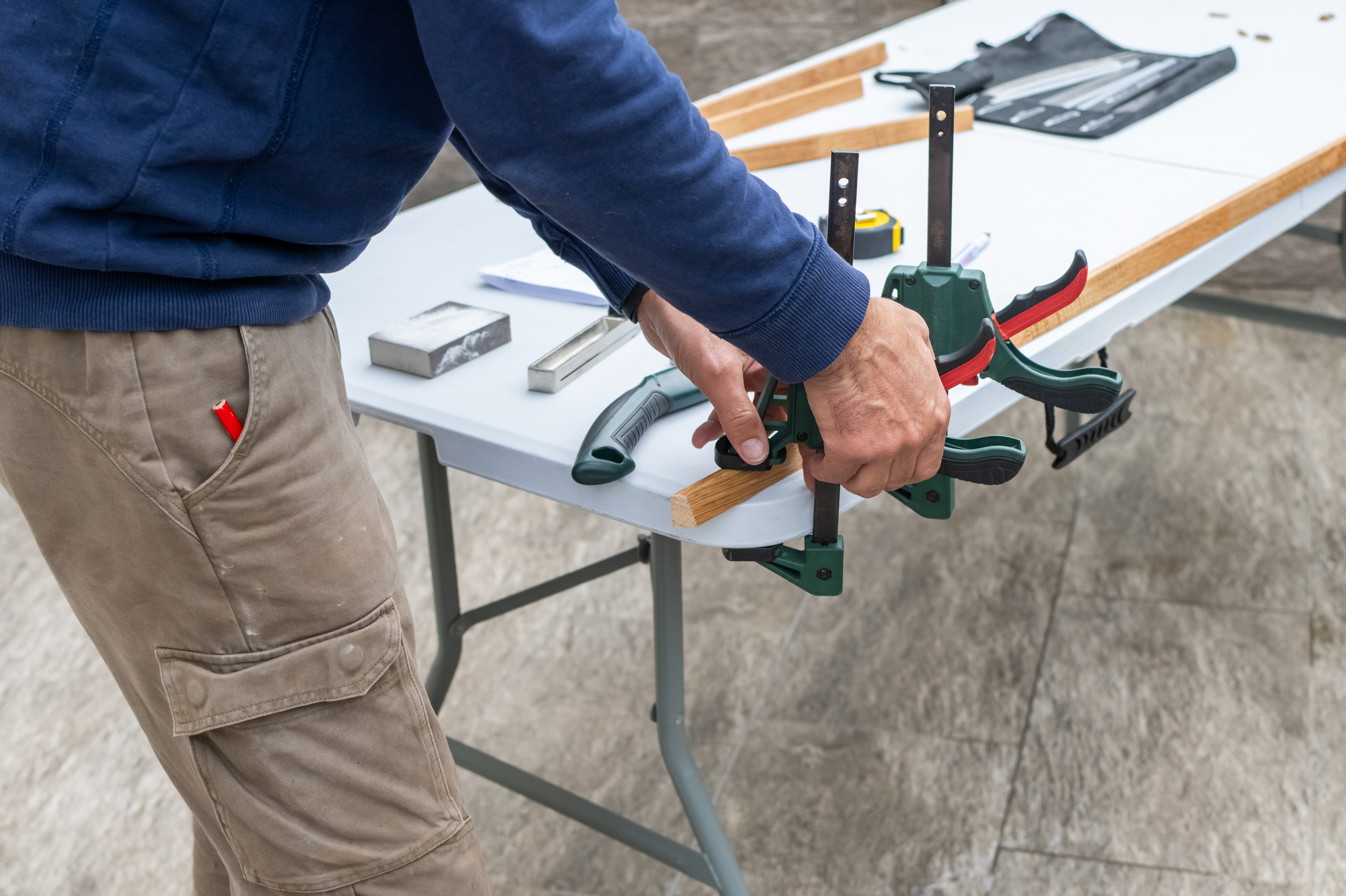 Worker demonstrating a green clamp vise on a workbench with tools