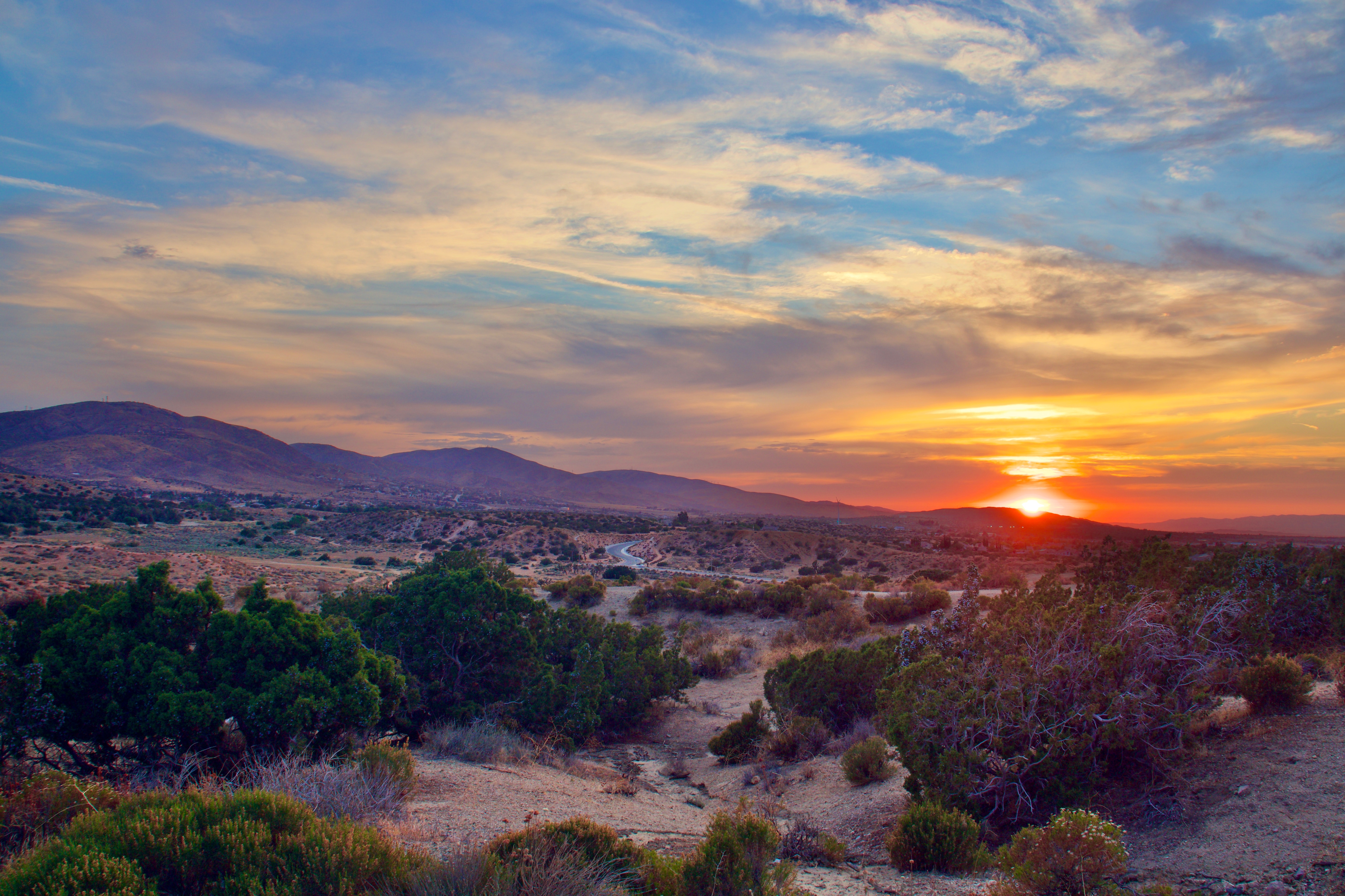 Sunset over arid landscape with river, sparse vegetation, and distant mountains