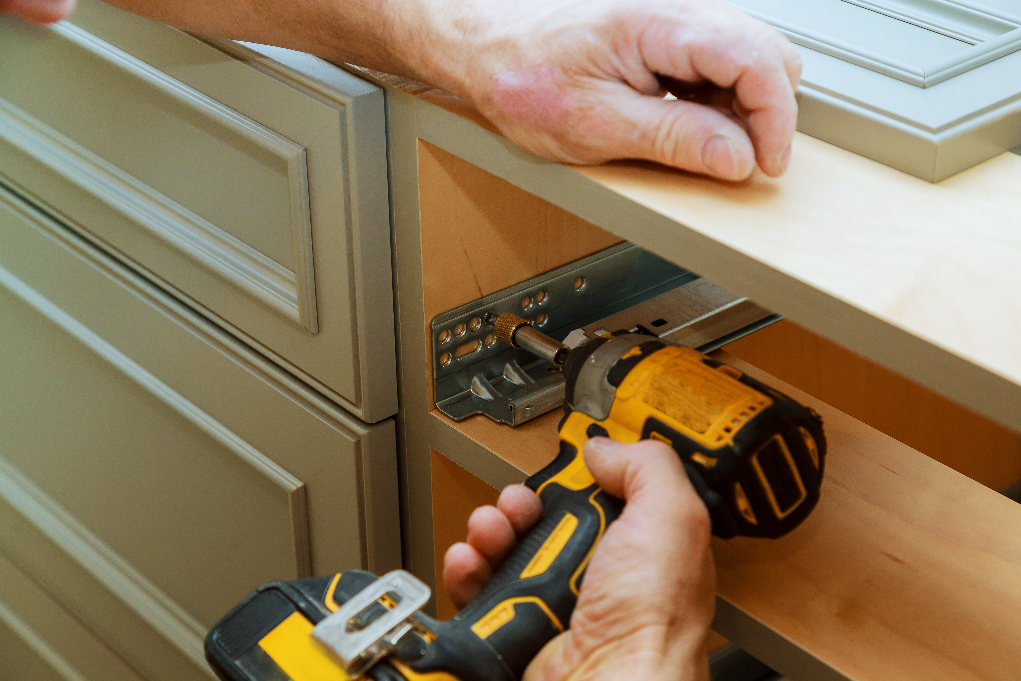 Technician using power drill to install dishwasher under kitchen cabinet