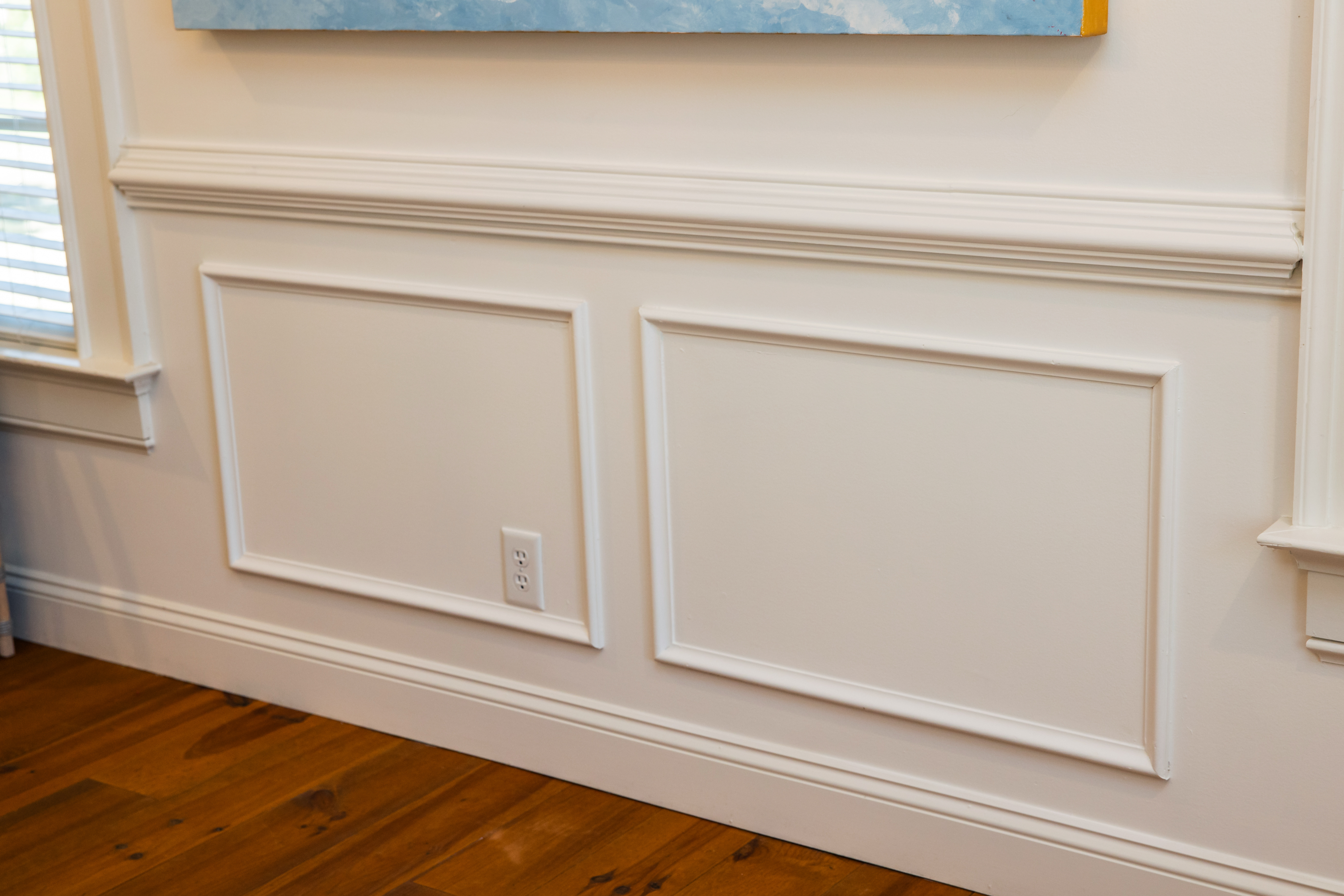 White wainscoting with two rectangular panels on cream wall above wooden baseboard